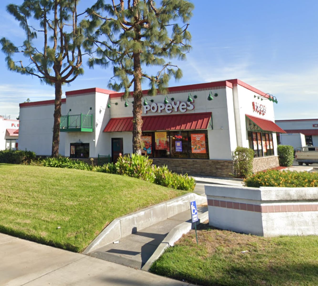 Front view from the street of a Popeye's Drive-Thru building with grass and trees in front