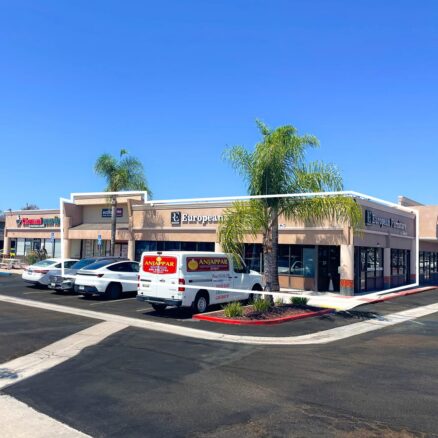 Single story building with salmon stucco, palm trees and cars parked in front