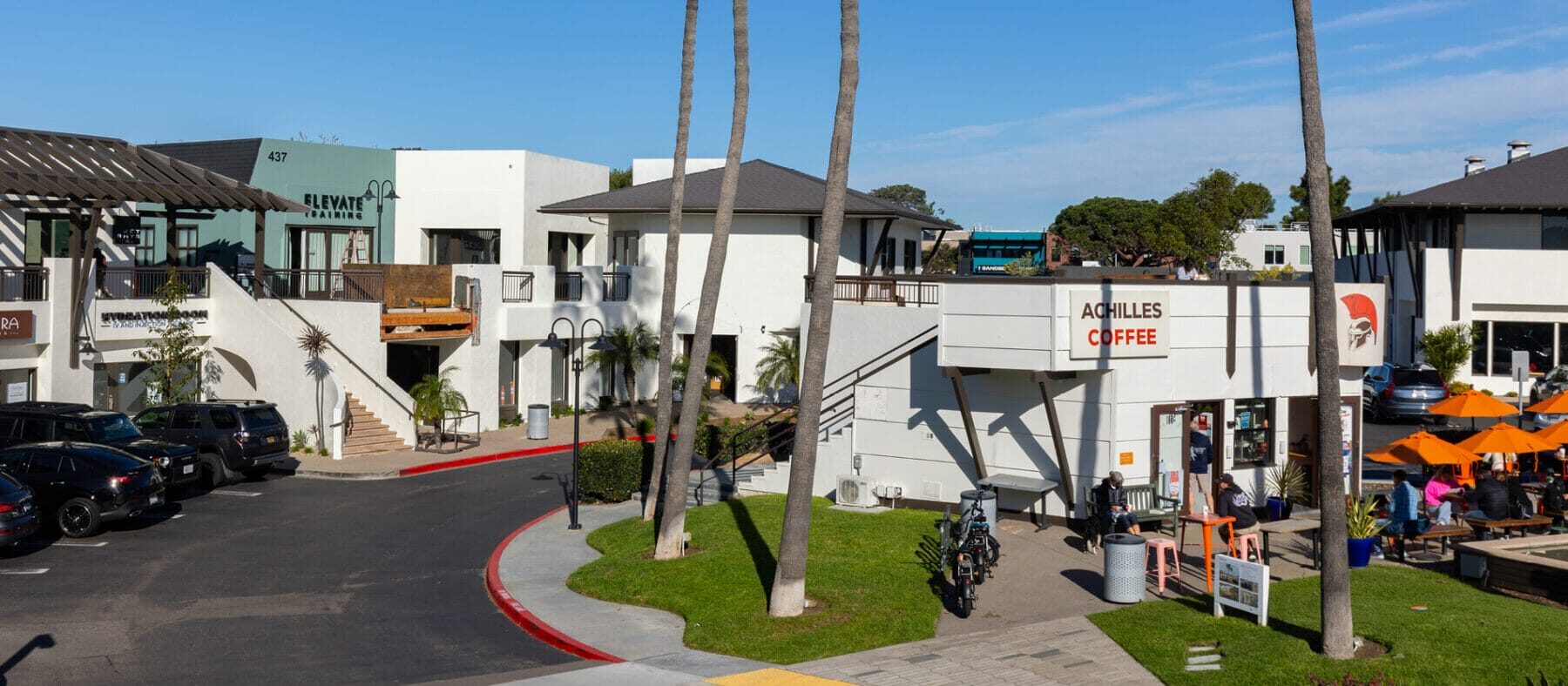 Straight on view of a shopping plaza with blue and white buildings and palm trees