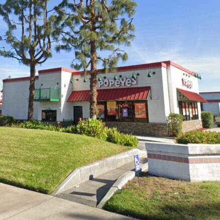Front view from the street of a Popeye's Drive-Thru building with grass and trees in front