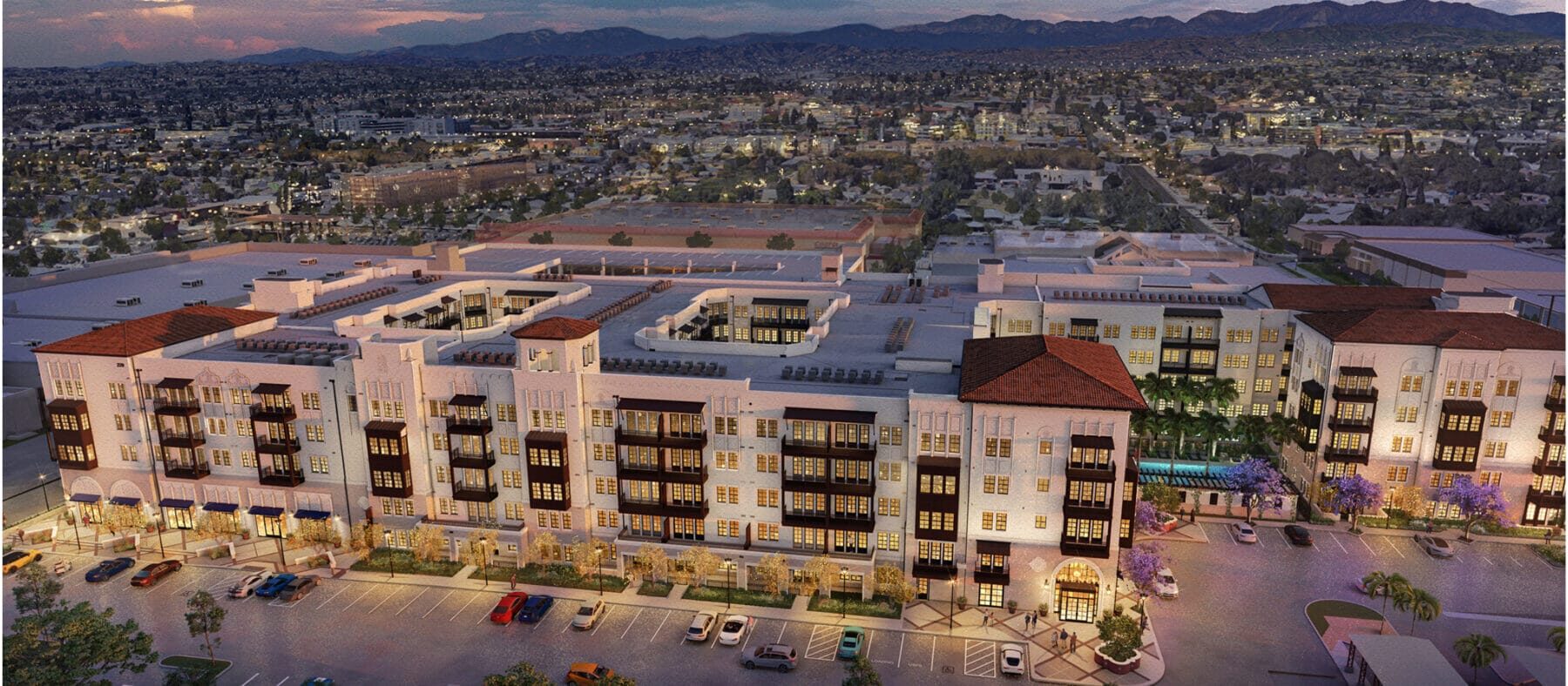 Several stories-high building with a sunset in the background. Building is white with some red tiling.