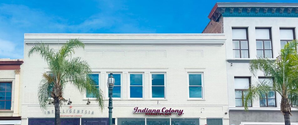 white two-story retail building, blue sky. Palm tree in front.