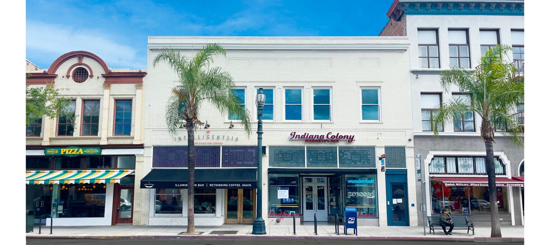 white two-story retail building, blue sky. Palm tree in front.