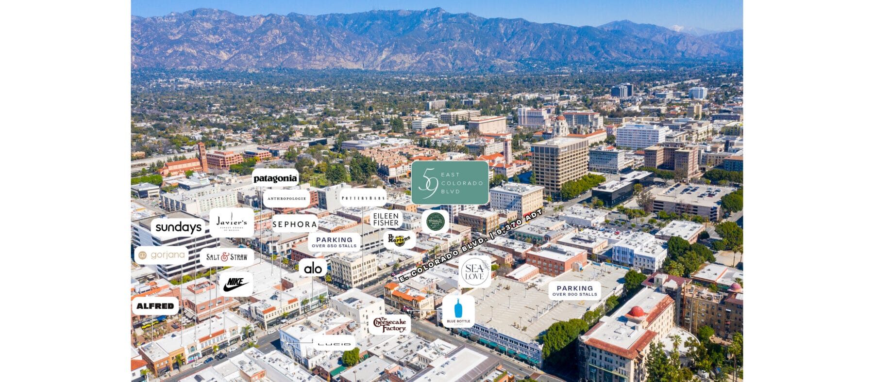 Aerial view of Colorado Blvd in Pasadena. Lots of buildings with mountains in background and blue sky.