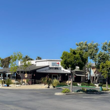 single story building of a restaurant with large trees surrounding it and a parking lot, with blue skies
