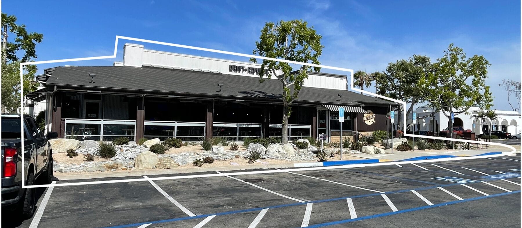 single story building of a restaurant with large trees surrounding it and a parking lot, with blue skies