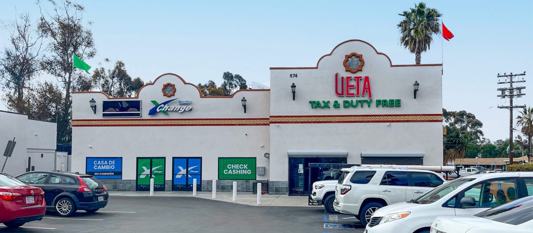 The building at 674 E San Ysidro Blvd viewed from the adjoining parking lot, suite B (Available Space) on the left and suite A (UETA Duty Free) on the right.