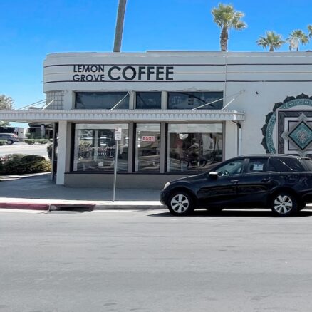 View of a single story building with multiple retailers, blue skies and palm trees in background