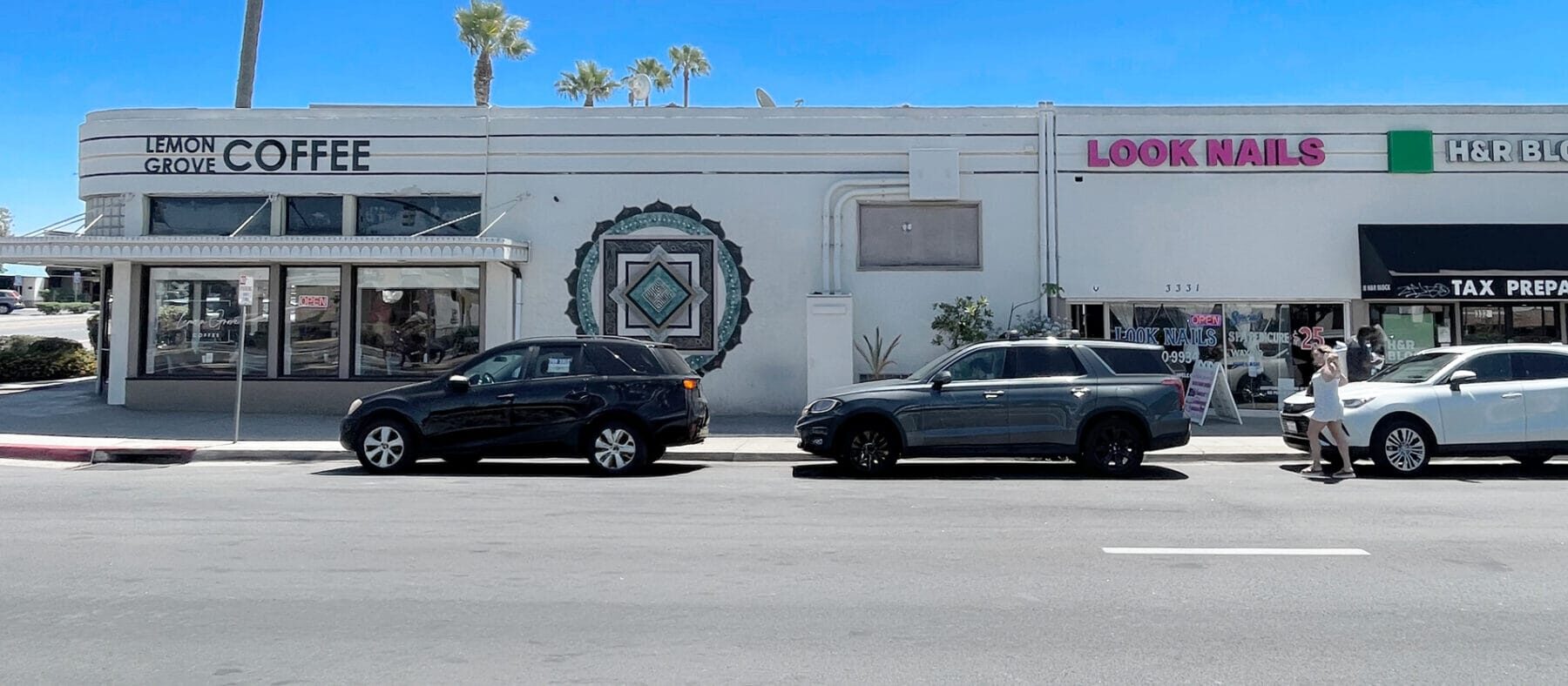 View of a single story building with multiple retailers, blue skies and palm trees in background