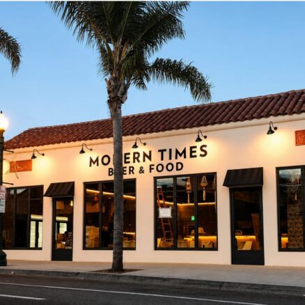 Single story beige building at dusk, with palm trees in the front