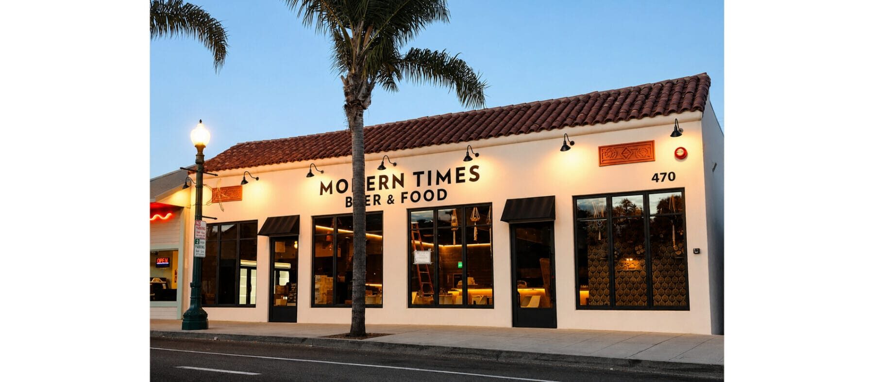 Single story beige building at dusk, with palm trees in the front