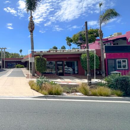 Front view of a single story red building with greenery in front and palm trees