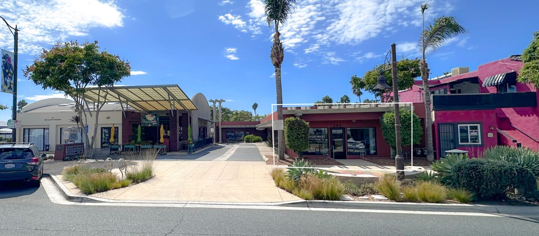 Front view of a single story red building with greenery in front and palm trees