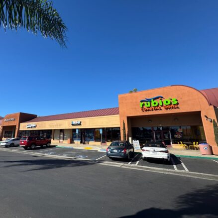 Strip mall center with tan and burnt Sienna buildings, blue sky and palm trees