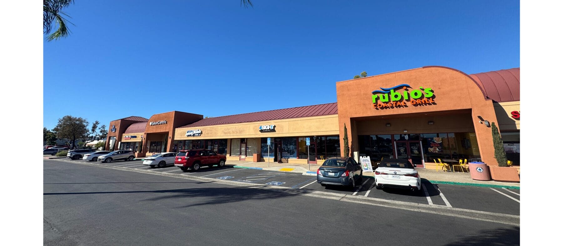 Strip mall center with tan and burnt Sienna buildings, blue sky and palm trees